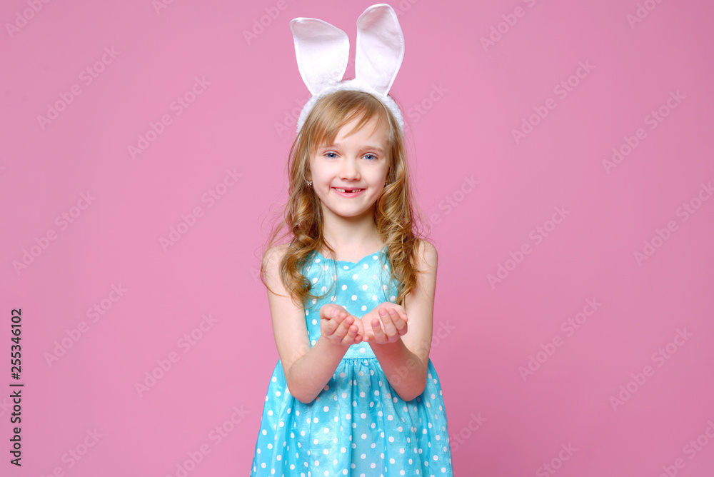 Cute little blonde girl in the shape of an Easter Bunny and a blue dress with a pea pattern holds her fingers . Concept of the celebration, advertising and fashion. happy Easter. Selective focus. Cute little blonde girl in the shape of an Easter Bunny and a blue dress with a pea pattern holds her fingers . Concept of the celebration, advertising and fashion. happy Easter. Selective focus.