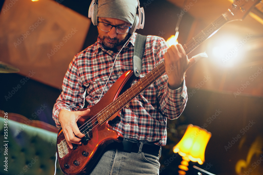 Obraz premium Focused Caucasian musician playing bass guitar with earphones on ears. Full length.