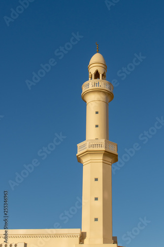 A spire and minaret of a white and orange mosque with a blue sky background.