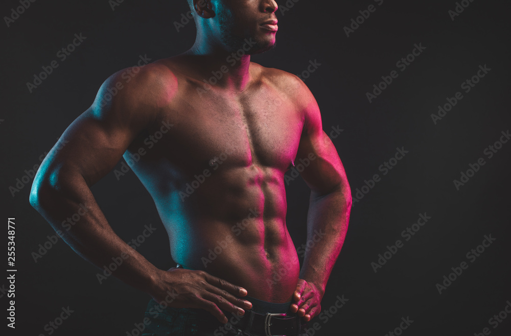Close shot of athletic African well built man with six pack abs posing shirtless at studio over dark background. - obrazy, fototapety, plakaty 