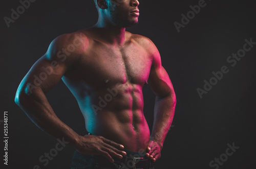 Close shot of athletic African well built man with six pack abs posing shirtless at studio over dark background.