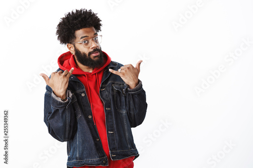 Swag in blood. Portrait of cool and stylish good-looking confident african-american male acting like star and popular person showing yolo gesture and looking self-assured at camera over gray wall