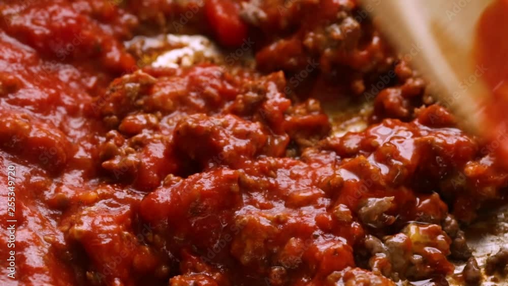 Close slow motion video of marinara sauce being stirred into browned beef and cheddar cheese hamburger meat in a pan while cooking with a wood spoon illuminated with natural lighting. Close slow motion video of marinara sauce being stirred into browned beef and cheddar cheese hamburger meat in a pan while cooking with a wood spoon illuminated with natural lighting.