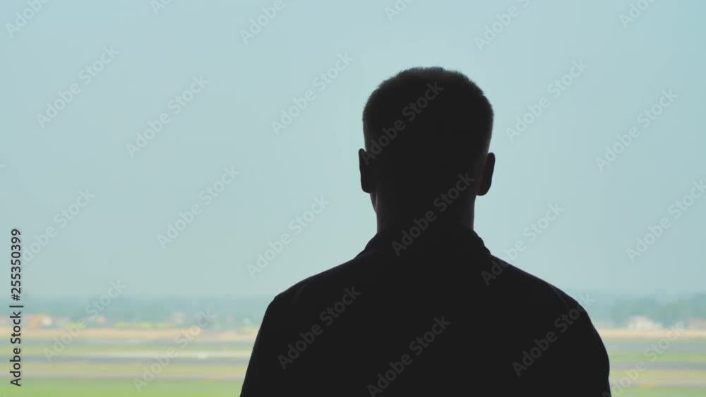 Silhouette of a young man watching the take-off of an airplane against a blue sky.