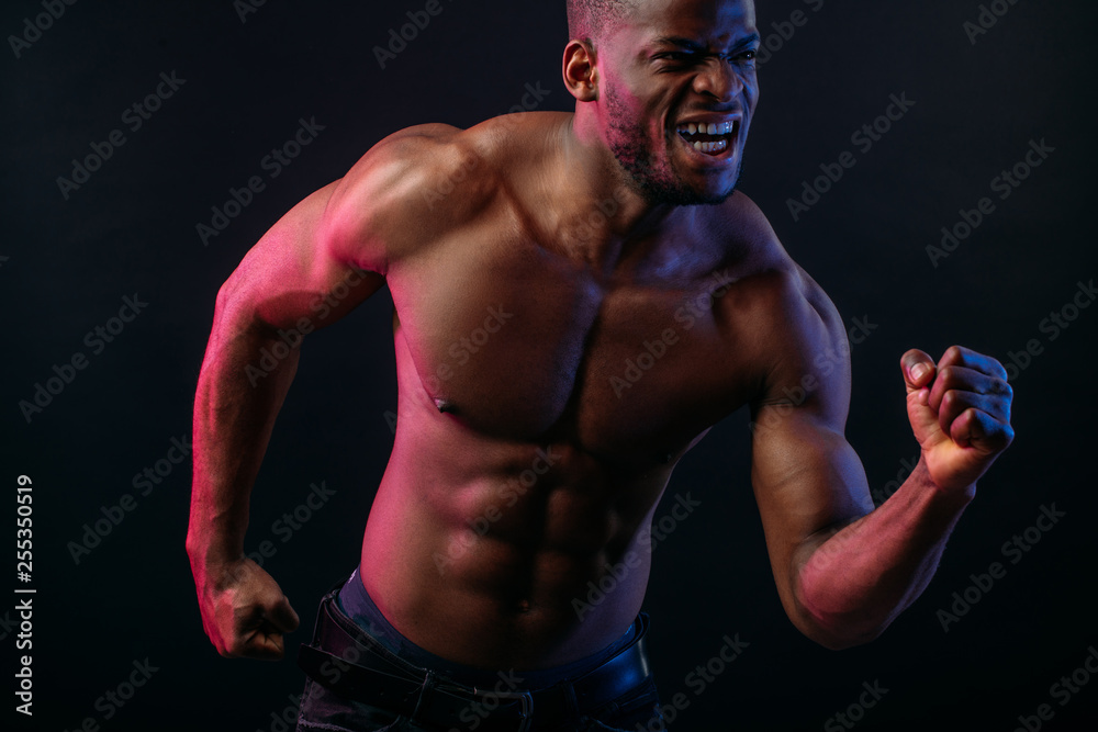 Attractive African male fighter or boxer posing shirtless, isolated over dark background. Toned and ripped muscular fitness man under dramatic low key lighting, copy space.