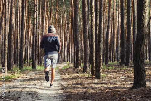 Man in hoodie has workout in a pine forest. Concept of morning matins jogging in outdoor © Alex