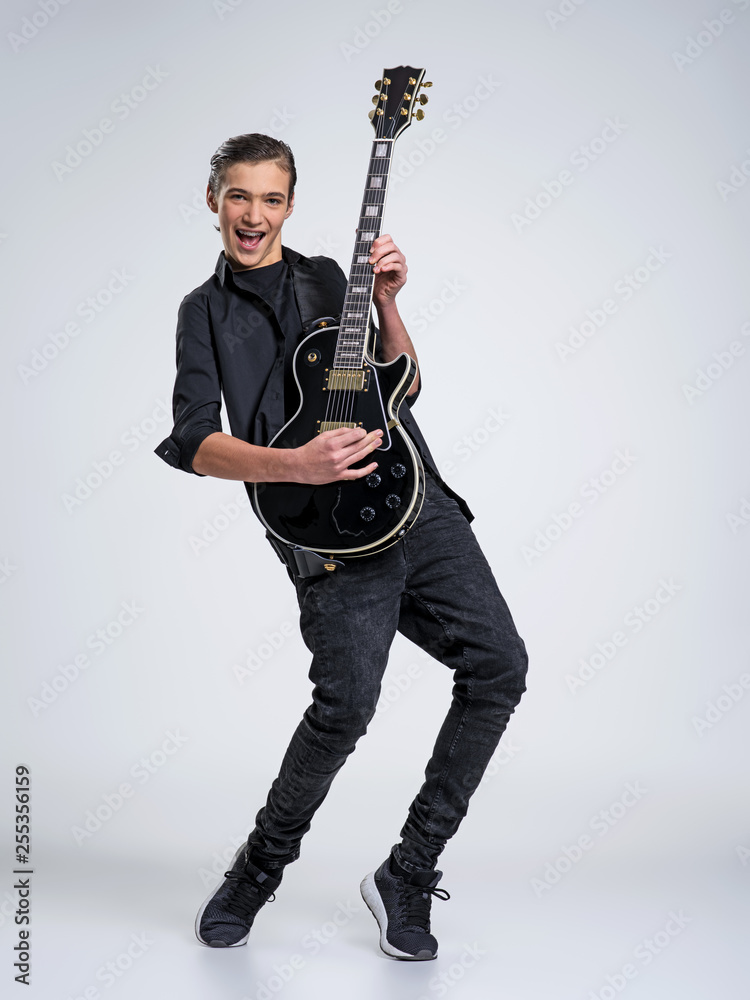 Naklejka premium Fifteen years old guitarist with a black electric guitar. Teenage musician holds guitar