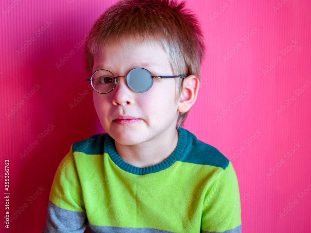 Portrait of funny child in new glasses with patch for correcting squint