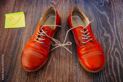 April Fool's day concept. Pair of red shoes on wooden background. Shoelaces tied together.