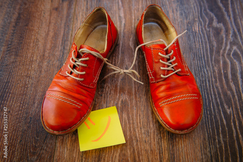April Fool's day concept. Pair of red shoes on wooden background. Shoelaces tied together.
