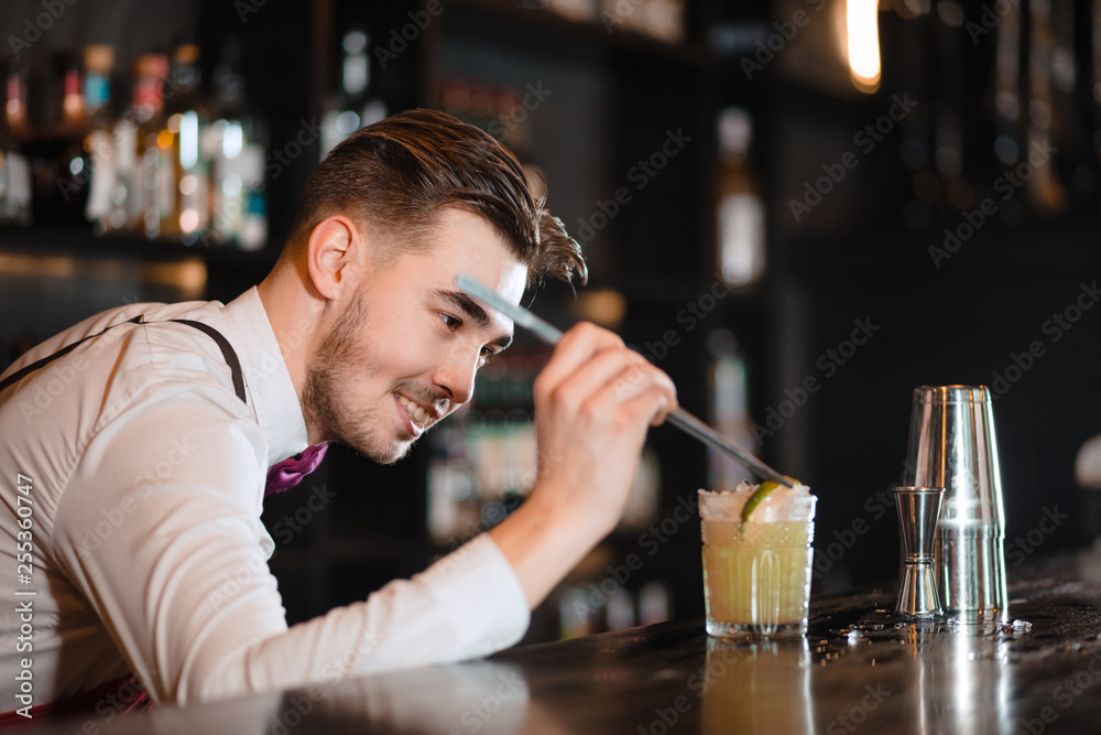 Bartender finishes decoration of his cocktail with ice cubes and lime slice