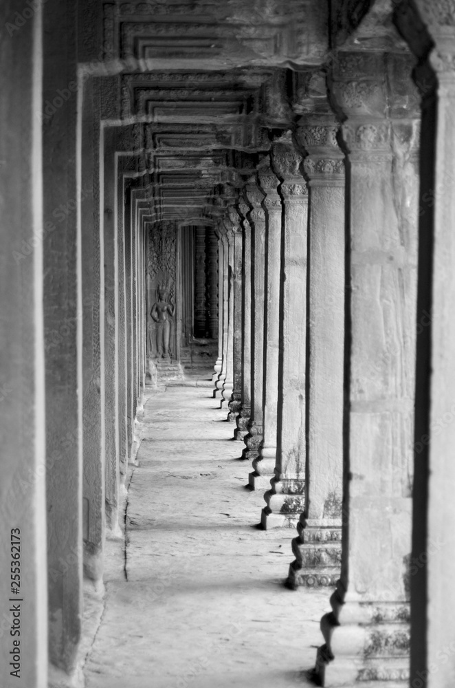 Stone pillars in a wat, or temple, in Cambodia line a corridor. At the end a carving of a female deity can just be seen. The photo is in black and white.