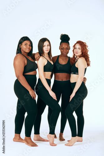 Group of women of different race, figure and size in sportswear standing together and laughing against white background.