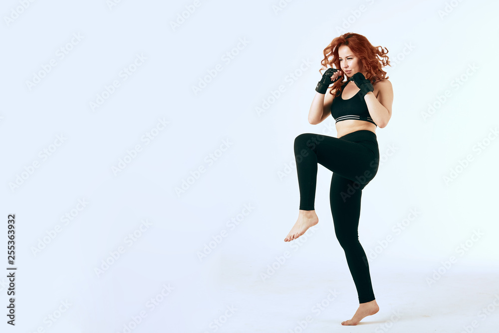 Female red-haired boxer in black sportswear doing worming exercise on white background