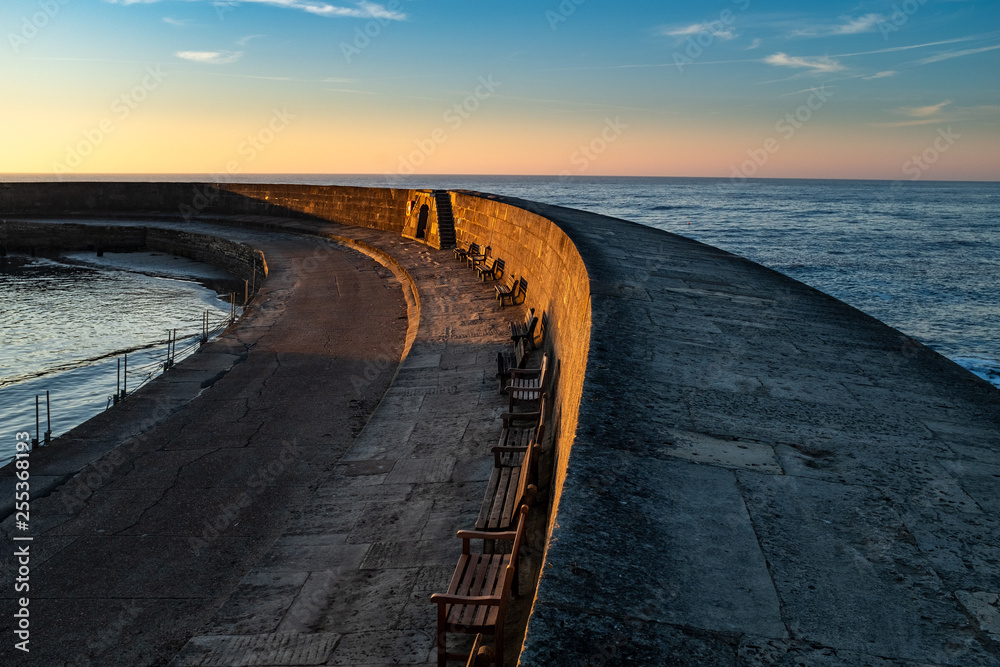 The Cobb at Lyme Regis sweeps out to sea, with the sun rising and the sky glowing