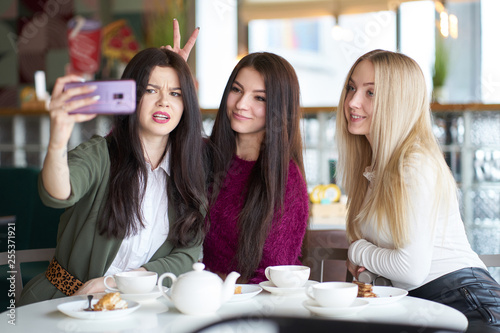 Girlfriends have fun in cafe, drinking tea and making selfie