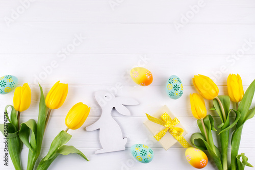 Happy Easter card. Frame with yellow tulips and easter eggs and bunny with copy space for text on white background. Top view