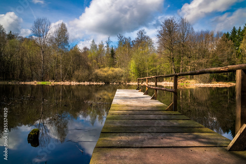 a pond with blue sky and clouds and a jetty leading into it © Sascha