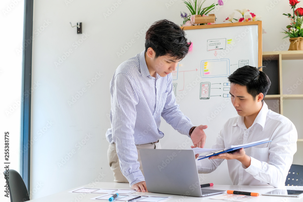 Obraz premium Two young asian man designer website applications consulting and planning work together. Job training to colleagues.