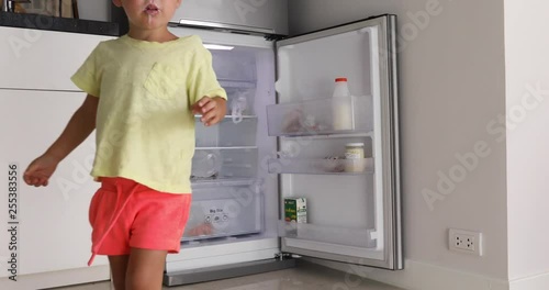 Boy with white mustache yogurt closes lid bottle which stands refrigerator photo