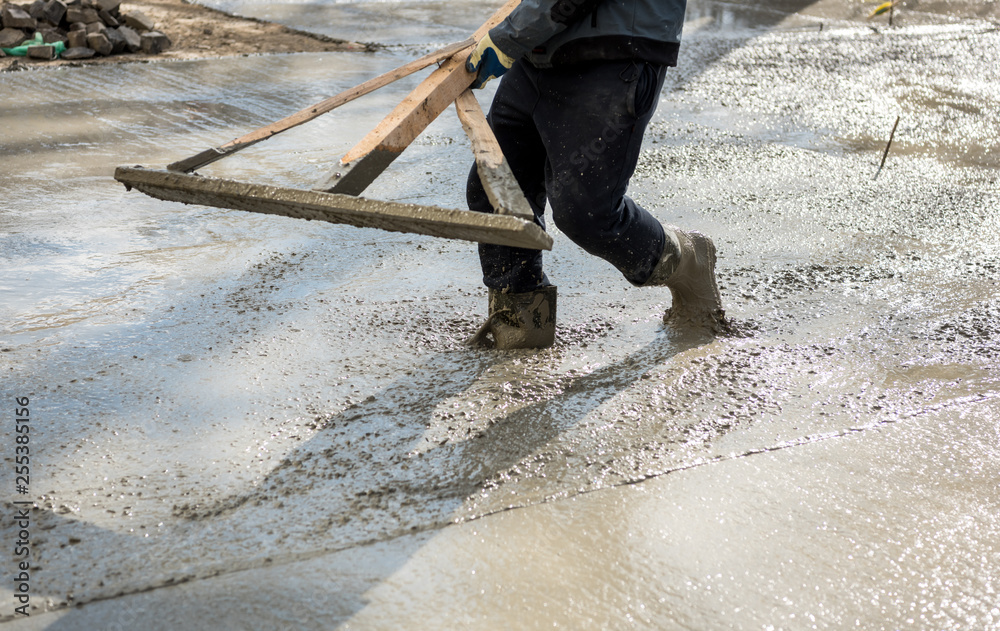 Worker leveling with wooden trowel the fresh poured concrete or cement at construction site. New urban road street project Worker leveling with wooden trowel the fresh poured concrete or cement at construction site. New urban road street project
