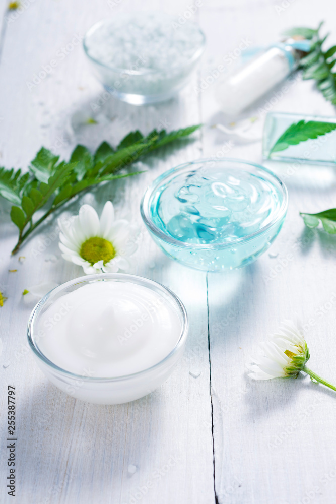 spa setting with cosmetic cream, gel, bath salt and fern leaves on white wooden table background