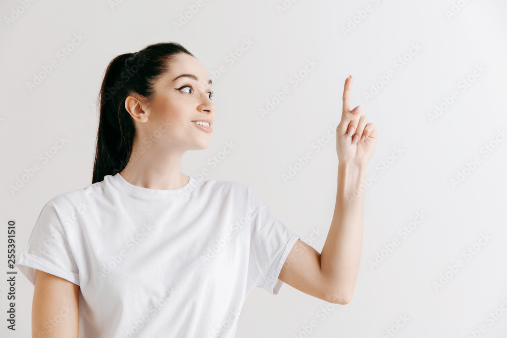 Happy woman standing and presenting something isolated on gray studio background. Beautiful female half-length portrait. Young emotional woman. The human emotions, facial expression concept. Happy woman standing and presenting something isolated on gray studio background. Beautiful female half-length portrait. Young emotional woman. The human emotions, facial expression concept.
