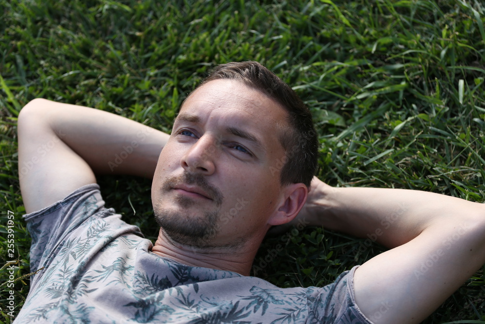 young man lies on the grass with his hands behind his head young man lies on the grass with his hands behind his head