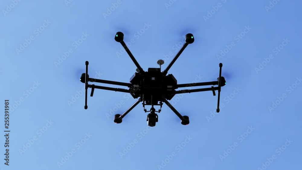 Hexacopter drone with a video camera hangs in the air against the blue sky. Bottom view. Hexacopter drone with a video camera hangs in the air against the blue sky. Bottom view.