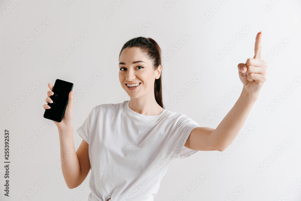 Portrait of a confident casual girl showing blank screen of mobile phone isolated over gray background at studio. Portrait of a confident casual girl showing blank screen of mobile phone isolated over gray background at studio.