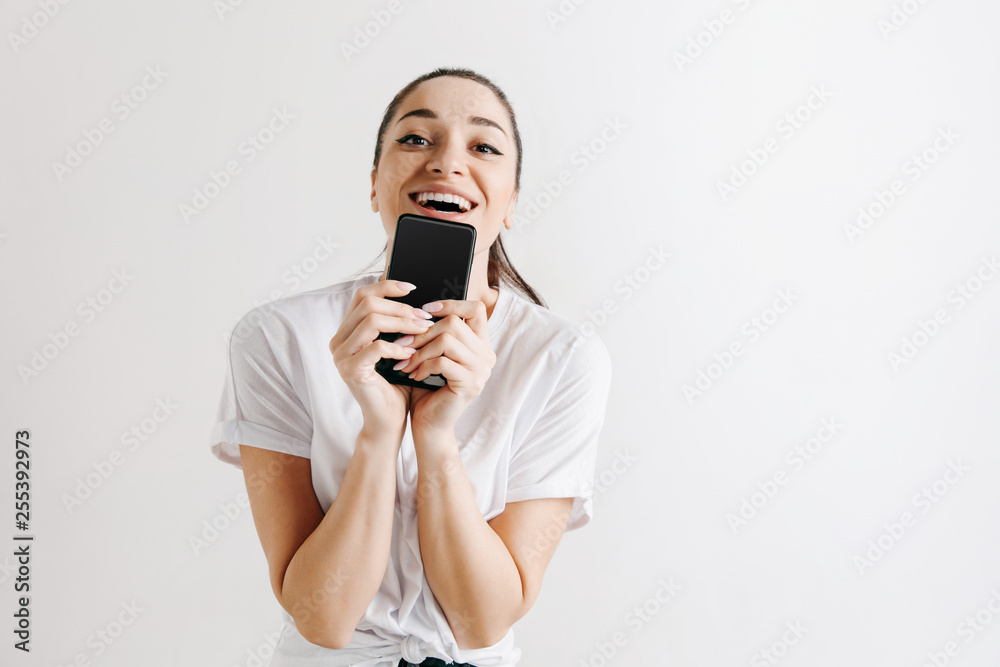 Portrait of a confident casual girl showing blank screen of mobile phone isolated over gray background at studio. Portrait of a confident casual girl showing blank screen of mobile phone isolated over gray background at studio.