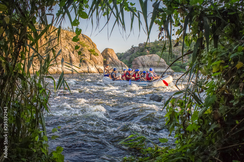 Mygiya / Ukraine - July 22 2018: Summer landscape stones in the river against the backdrop of a floating raft. Rafting on the  Pivdennyi Buh River photo