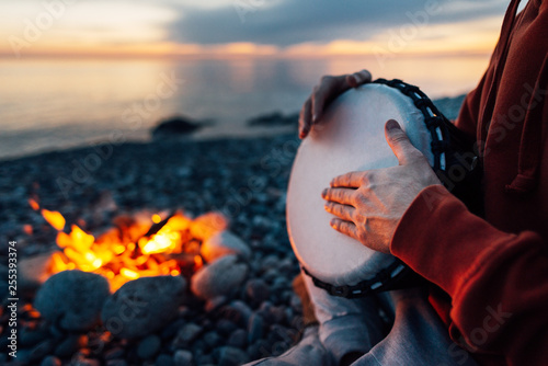 percussionist plays djembe on the seashore near fire, hands close up photo