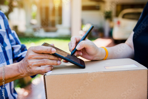 woman appending signature sign on smartphone after accepting receive boxes from delivery man at home, photo