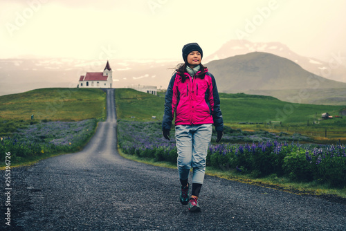 Woman traveler travel to Ingjaldsholl church in Hellissandur, Iceland in the field of blooming lupine flowers with background of Snaefellsjokull mountain. Beautiful sunny scenery of summer in Iceland. photo