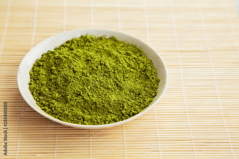 Powdered matcha green tea in a plate on a bamboo table Powdered matcha green tea in a plate on a bamboo table