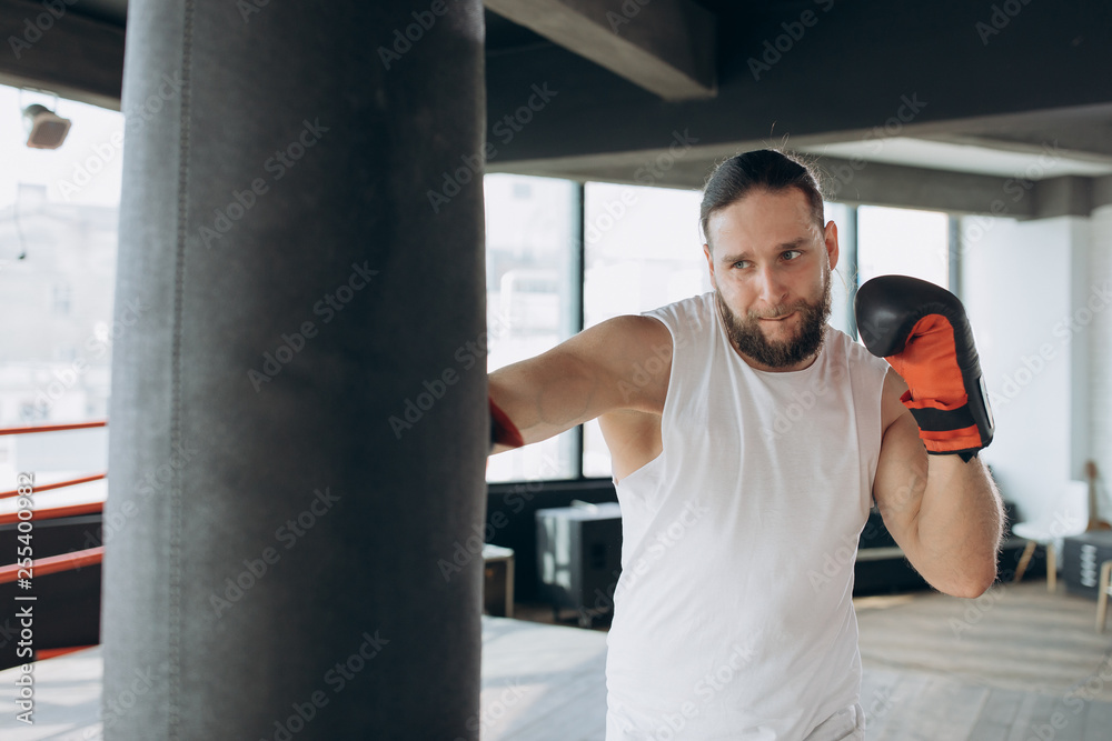 Boxer hits punching bag in gym in slow motion. Young man training indoors. Strong athlete in gym. Sport concept