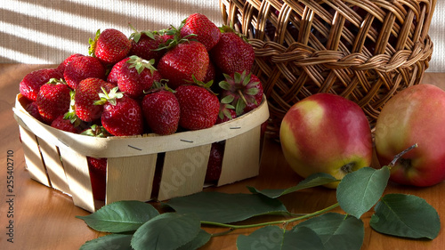Ripe strawberries in a basket, on a morning table with apples and cherries