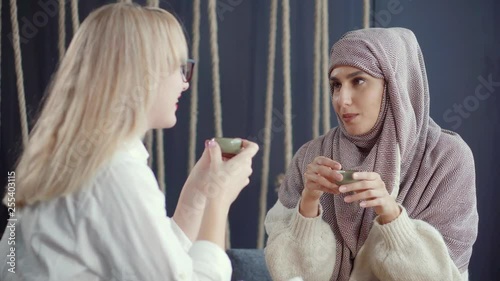 Religious muslim woman and her female secular blonde friend are talking friendly