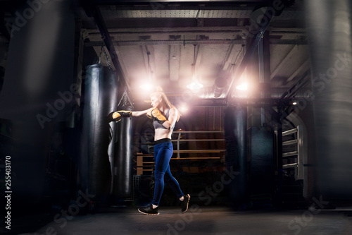 Athlete woman boxer practicing near bag, ring in gym