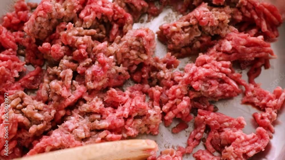 Close slow motion video of breaking apart hamburger in a pan for cooking with a wood spoon illuminated with natural lighting. Close slow motion video of breaking apart hamburger in a pan for cooking with a wood spoon illuminated with natural lighting.