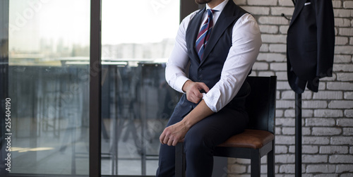 Man in custom tailored suit, vest sitting and fixing his cufflinks