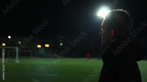 The guy is watching football training at the evening stadium