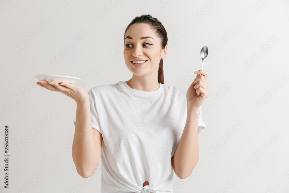 Young fun crazy brunette housewife with spoon isolated on white background. Housekeeper woman holding white empty plate. Copy space advertisement. Young fun crazy brunette housewife with spoon isolated on white background. Housekeeper woman holding white empty plate. Copy space advertisement.