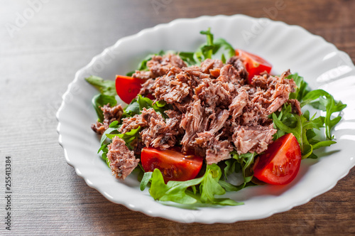 Tuna salad with arugula and tomatoes in white plate on wooden table background