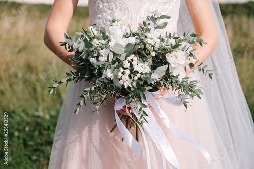 wedding bouquet of white flowers with ribbons in the hands of the bride