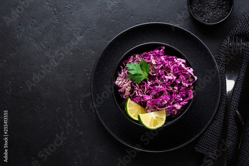Salad of purple Peking cabbage with olive oil, lime and black sesame seeds in ceramic plate on dark concrete background.