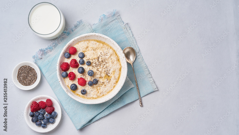 Oatmeal with berries, chia, maple syrup and glass of milk on blue light background. Top view, copy space. Long width banner. Healthy diet breakfast Oatmeal with berries, chia, maple syrup and glass of milk on blue light background. Top view, copy space. Long width banner. Healthy diet breakfast