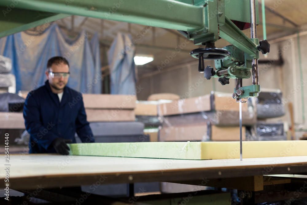 Young man in a furniture factory is cutting the foam for the sofa Young man in a furniture factory is cutting the foam for the sofa