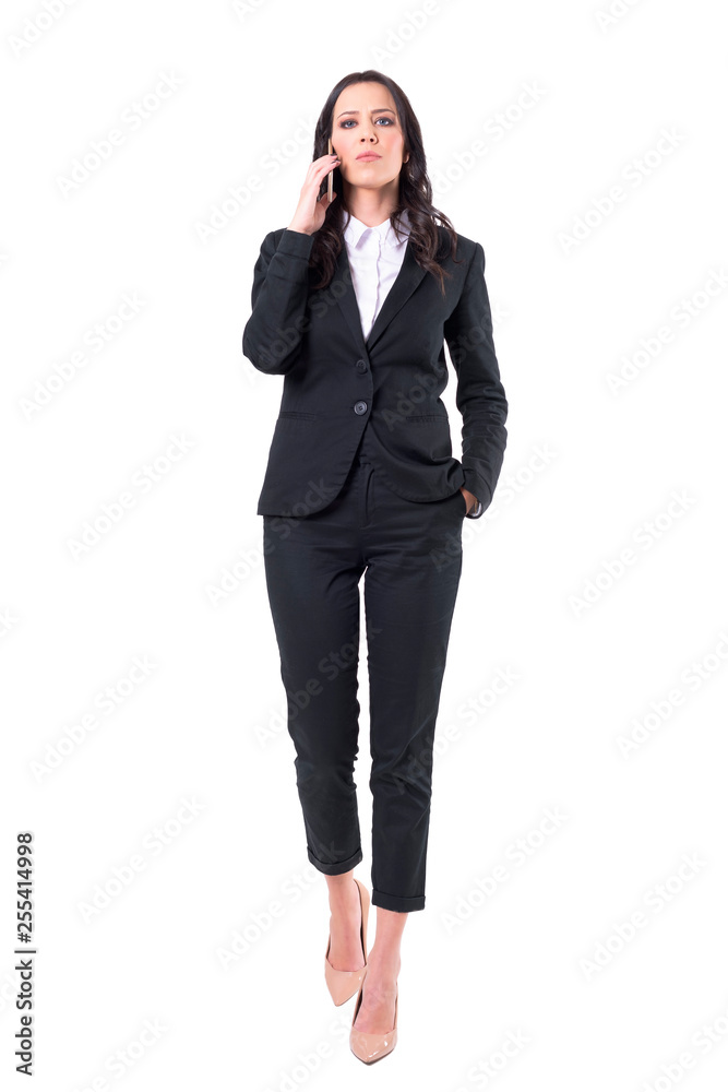 Serious attitude bossy business woman talking on the mobile phone walking towards camera. Full body isolated on white background. Serious attitude bossy business woman talking on the mobile phone walking towards camera. Full body isolated on white background.